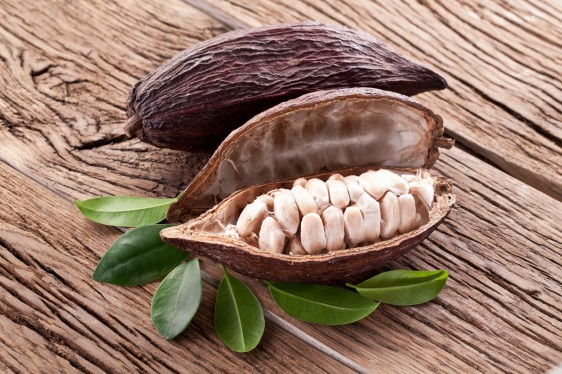 fruto de Cacao en una mesa sobre sus hojas abierto a la mitad mostrando las semillas