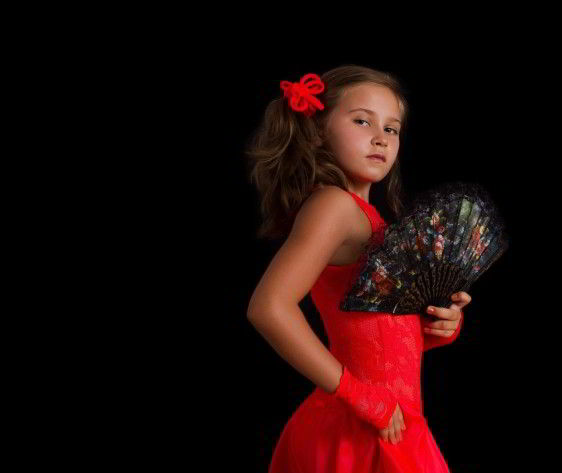 Niña con vestido rojo y abanico en postura de baile flamenco