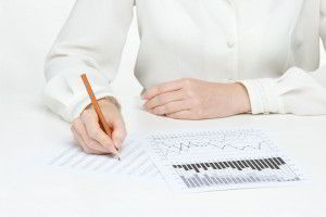 Acercamiento de la mano de una persona con camisa blanca escribiendo sobre graficas