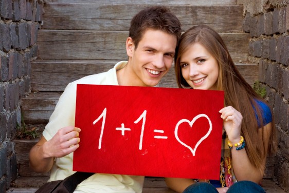 Dos jovenes con letrero rojo con texto 1 + 1 igual a amor