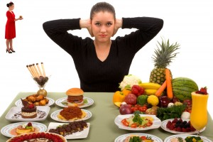 Mujer tapandose los oidos con un diablito a su derecha y con una mesa con comida enfrente a la isquierda pasteles hamburgesas a la derecha drutas y verduras