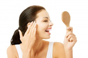 Mujer de cabello negro con un acercamiento a su rostro mirando un espejo y rocando su rostro y sonriendo