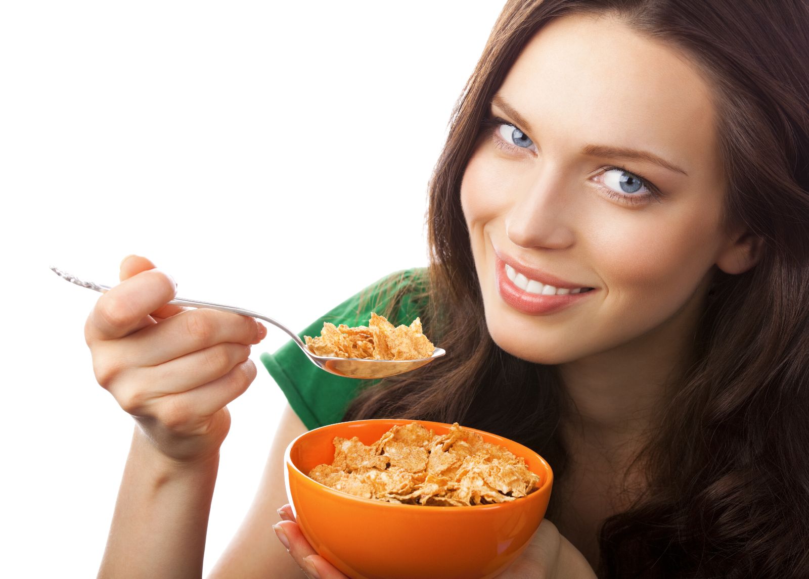 Mujer sonriendo con camisa verde y con una cuchara en la mano, con la otra sosteniendo plato hondo naranja que contiene cereal