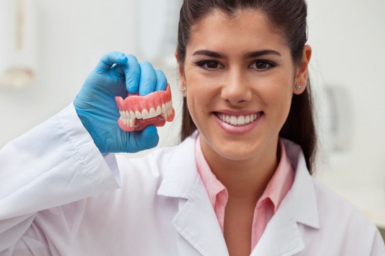 Dentista con bata blanca sonriedo y sostenido una muestra de dientes en la mano