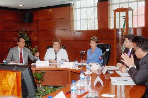 Mercedes Juan y funcionarios de la Red Mexicana de Municipios sentados en una mesa de madera atrás un muro de madera