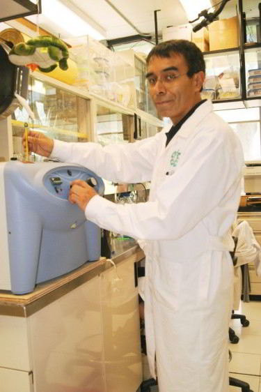 Doctor Jaime García Mena en bata blanca de pie operando un equipo de laboratorio