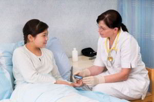 Doctora sentada con instrumento en la manos tomando el brazo de una paciente en cama