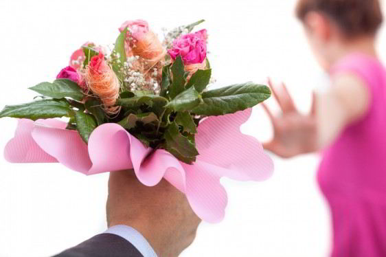 Mano de un hombre con rosas y una mujer vestida de rosa con la mano en alto en señal de rechazo