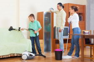 Niño aspirando hombre quitando polvo y mujer trapeando en imagen de concepto de labores domésticas