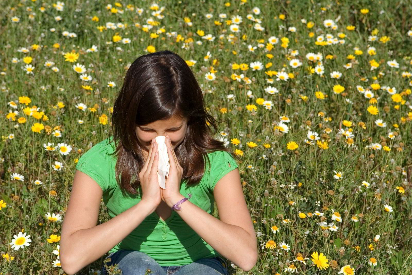Niña con camisa verde, estornudando y sentada en un campo de flores