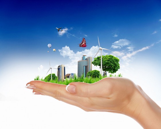Mano de una mujer sostiene un paisaje de una ciudad con energia eólica, foto celdas y edificios atrás un cielo azul