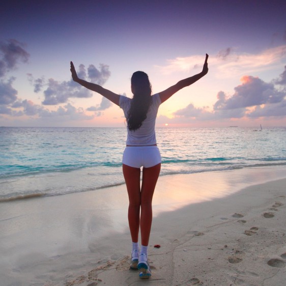 Una mujer con los brazos abiertos en una playa al amanecer