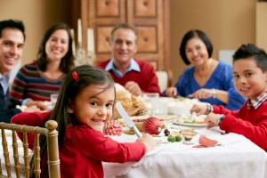 Acercamiento a niña sentada en la mesa sonriendo al fondo desenfocados nilo y adultos en la mesa comiendo