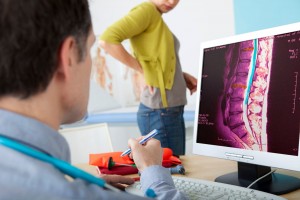 Médico observando en l pantalla una columna vertebrl al fondo se observa desenfocada una mujer de pie