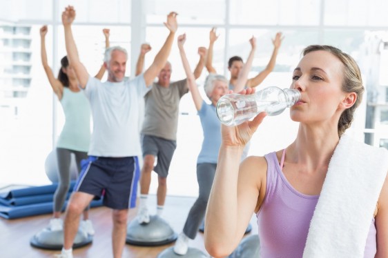Mujer en ropa deportiva tomando agua de uina botela transparente en el fondo personas haciendo ejercicio