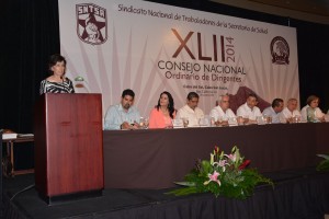 Marcela Velasco González en un podium atras una mesa con personas y un letrero logotipo del XLII consejo nacional ordinario de dirigentes