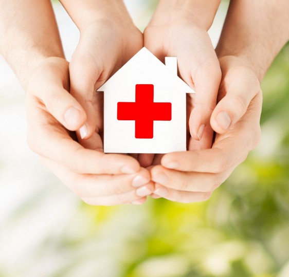 hands holding paper house with red cross