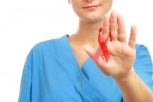 Acercamiento a una mano de una cirujana en bata azul con la mano en señal de alto con un listón rojo