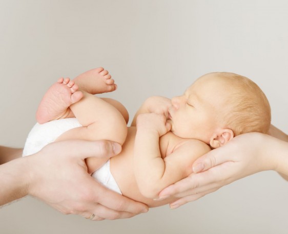 Acercaminto a un bebé sotenido en la manos de su padre y madre