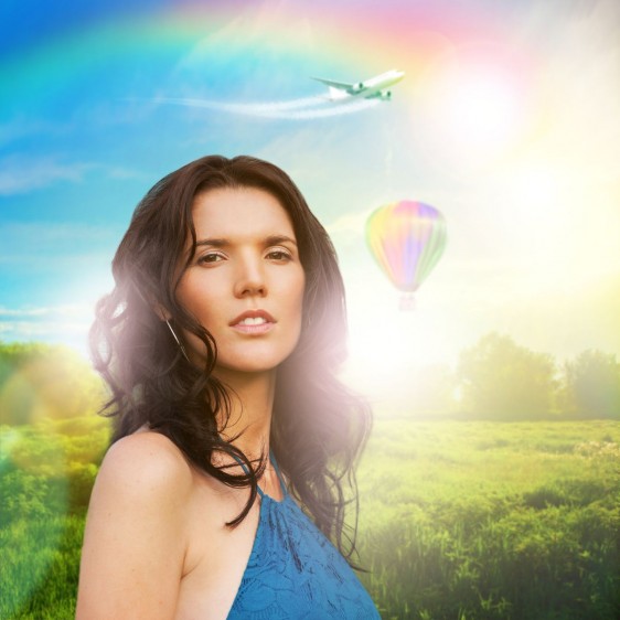 Mujer con vestido azul atras un campo verde con un globo aerostatico y un arcoiris