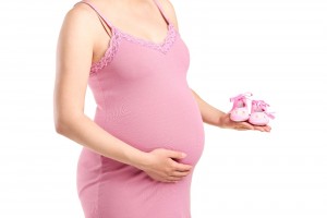 Acercamioento a mujer embarazada con cestido rosa y zapatitos de bebé en la mano