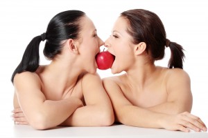 Dos mujeres comiendo una manzana que se encuentra entre sus bocas
