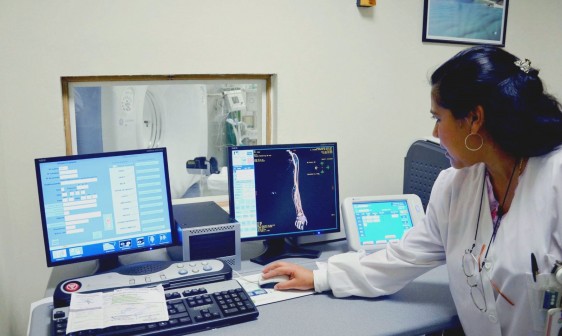 Doctora observando resultados en una pantalla de computadora al fondo un equipo de resonancia magnetica