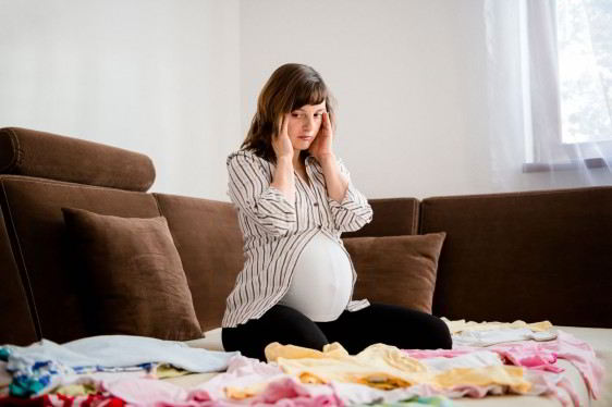 Mujer embarazada sentada n una cama con expresión de preocupación