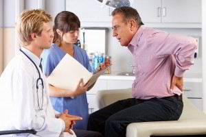 Adulto mayor se toca la espalda médico lo observa al lado de una enfermera se encuentran en un consultorio médico