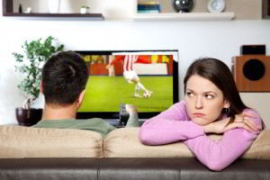 mujer aburrienda, mientras su compañero viendo deporte