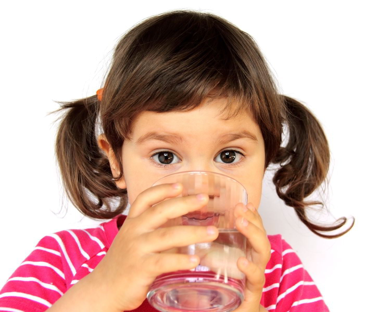 Niña pequeña von trenzas y camisa rosa con rayas blanca bebiendo un vaso con agua