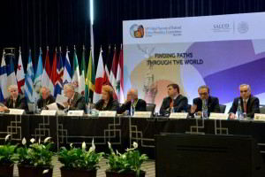Personas sentadas en una sala atrás banderas de países y letrero "10 Cumbre Global de Comisiones Nacionales de Ética y Bioética"