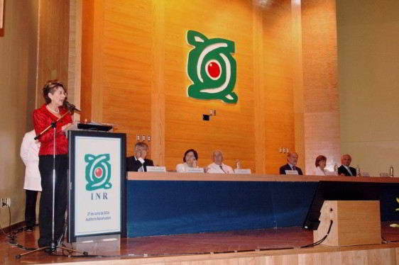 Mercedes Juan en un podium atras personas sentadas en una mesa