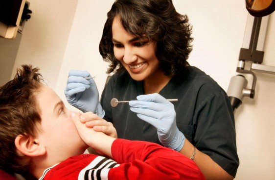 Dentista con aparatos en su mano con un niño sentado tapándose la boca