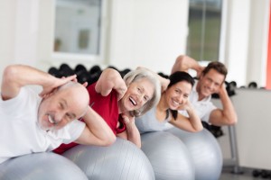 Mujer mayor sonriendo en un ginnacio con otras personas haciendo ejercicio sobre una pelota