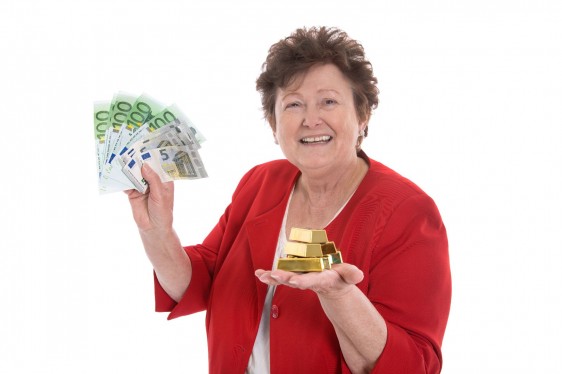 Mujer mayor feliz con billetes en la mano izquierda y barrras de oro en la mano derecha
