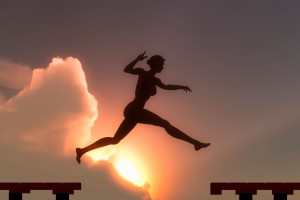 Silueta de una mujer saltando para alcanzar un escalón al fondo una puesta de sol