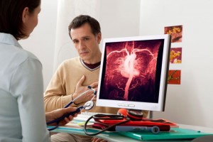 Hombre en consulta con doctora que observa una pantalla con ilustración del sistema cardivascular