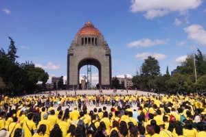 Personas con camiseta amarilla agarradas de la mano enfrente del monumento a la revolución
