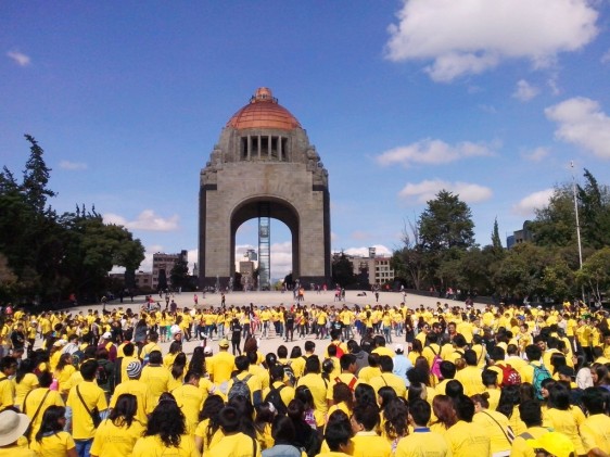 Personas con camiseta amarilla agarradas de la mano enfrente del monumento a la revolución