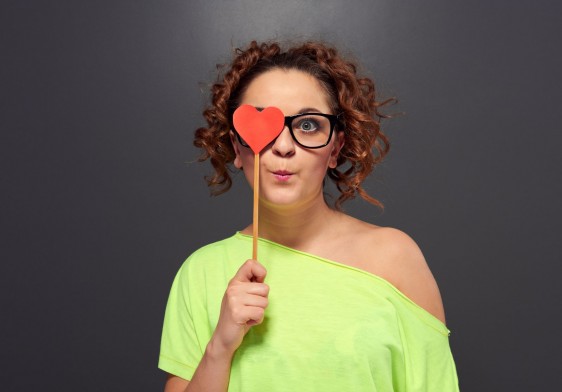 Mujer con gafas se cubre un ojo con recorte de corazón rojo