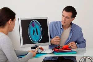 Doctora observa pantalla de cmputadora con imagen de cerebro al lado la acompaña un paciente