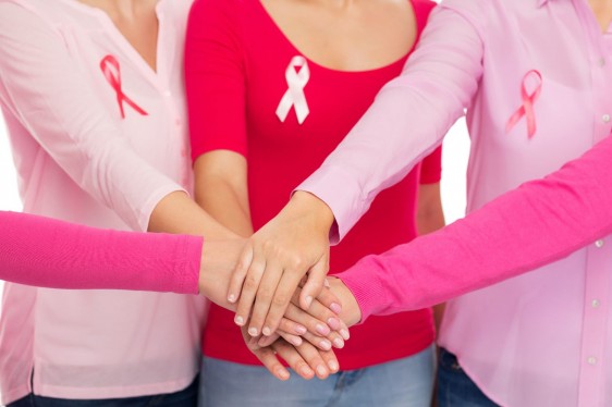 Acercamiento a manos de mujeres juntas cada una lleva el listón de cáncer de mama
