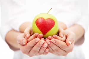 Acercamiento a las manos de una mujer que sostiene las manos con las palmas arriba de un niño que sostiene una manzana verde que contiene un corazón rojo