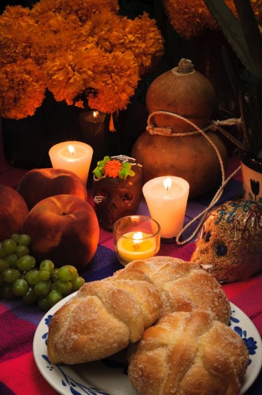 Ofrenda del día de muertos, pan de muertos, uvas, velas, amaranto calaveras y flores en el fondo