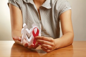 Mujer sostiene en sus manos recorte de papel con forma de personas y un listón rojo del SIDA