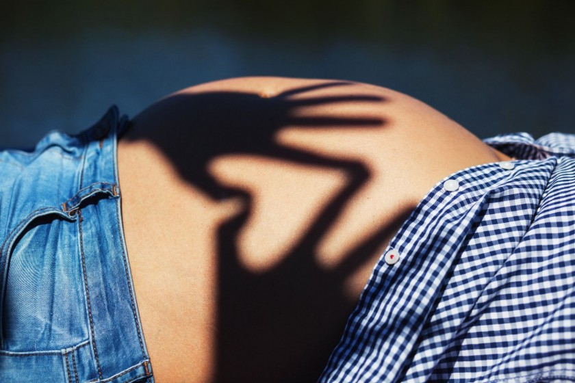 Acercamiento al estomago de mujer embarazada en donde se proyecta una sombra de dos manos que forma un corazón