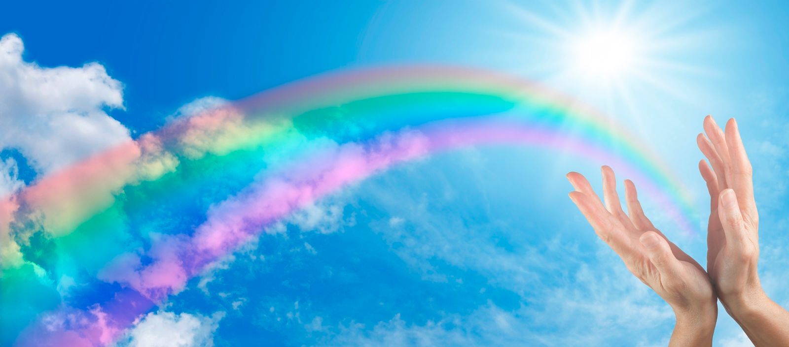 Manos abiertas hacia el cielo con un arco iris en el fondo