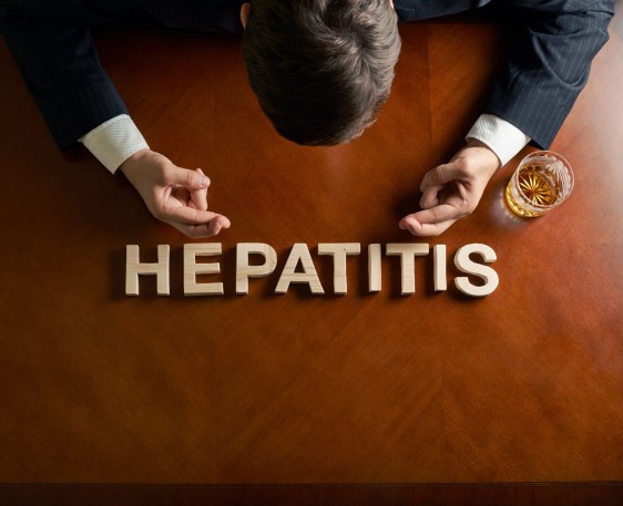 Persona sentada en una mesa con letras que forma la palabra HEPATITIS