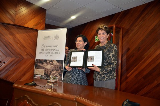 Patricia Cravioto  Galindo y Mercedes Juan sosteniendo en sus manos la Estampilla postal conmemorativa al 85 Aniversario del Edificio de la Secretaría de Salud